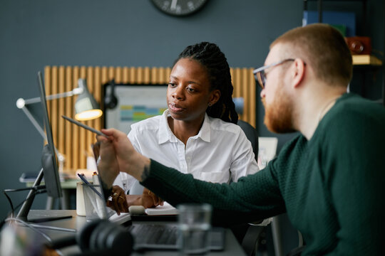 Colleagues discussing project at modern office, one African American woman and one Caucasian man, using tablet device, brainstorming ideas and collaborating on task