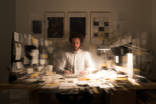 Conceptual image of a stressed man at a desk with motion blur to depict overwhelm and multitasking