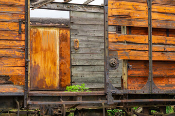 Old, weathered freight wagon with decayed wooden walls and rusty metal elements. The photo captures construction details and signs of aging, perfect for illustrating themes related to industry, railwa