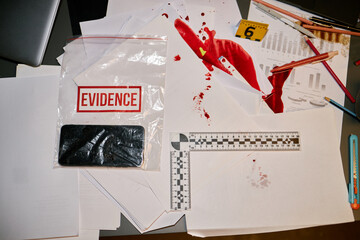 Evidence bag containing phone with spilled blood on papers and crime scene marker nearby, along...
