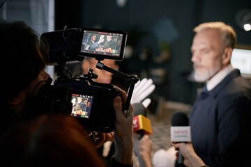 Businessman engaged in press interview surrounded by media members holding microphones and cameras...