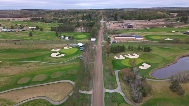 Main street with driving cars between TPC Toronto at Osprey Valley in Alton, Canada. Aerial forward wide shot. Green forest trees and fields in suburbia.