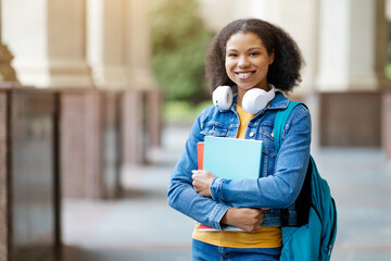 African american female student with backpack and workbooks posing outdoor at university campus,...