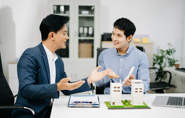 Two businessmen discuss and sign a real estate contract with housing models on a desk for concepts of property, investment