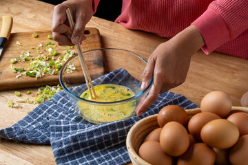 person is beating raw eggs with spring onions with wooden chopsticks