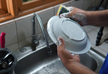 Man's hands washing dirty dishes holding a soap suds sponge in the kitchen