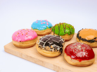 Assorted colorful donuts with various toppings displayed on a wooden board