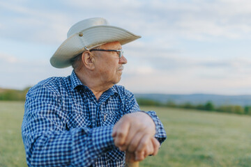 Fototapeta premium Elderly Cowboy Farmer Stands Still as Sunset Falls on the Farmland