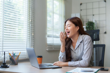 Obraz premium Young businesswoman yawning while working on laptop in office