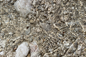 close-up of white and gray stones submerged in transparent river water with vivid light reflections and natural patterns