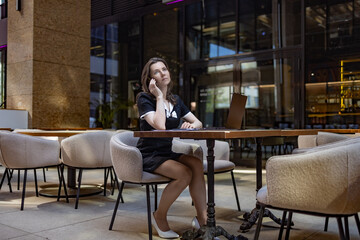 A business-style business lady is working on a laptop in an outdoor cafe. Conducts negotiations by phone