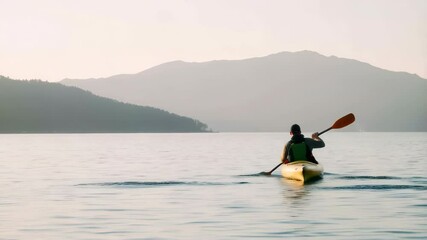 Back view of man canoeing in the sea with mountains in the background. Outdoor adventure and nature exploration concept