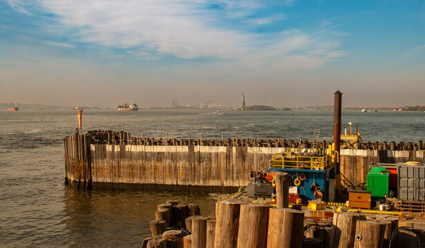 Estatua de la libertad desde el sur de la isla de Manhattan, NYC, USA. Paisaje de Upper Bay en Nueva York con los pilones de madera del muelle al sur del distrito financiero. Al fondo New Jersey.