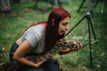 A girl with red hair interacts closely with a boa constrictor, showcasing calmness and connection...