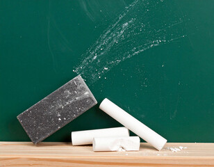 A dusty chalk eraser resting under a green blackboard alongside pieces of broken white chalk.