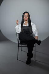 Confident woman with long black hair posing in studio lighting. Monochrome outfit, bold red lips, minimal background. Strong, stylish and professional portrait.