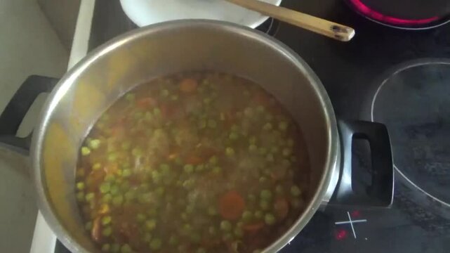 Cooking peas in a saucepan. A woman's hand opens the lid of a saucepan where vegetarian food is being cooked. Green peas, onions and carrots are stewed in a saucepan. Natural food ingredients for heal