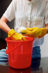 Woman in yellow gloves cleaning bucket of water with sponge in front of red table © SHOTPRIME STUDIO