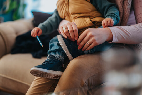 A parent assists their child in putting on shoes, focusing on care and attention, highlighting the bond and interaction. The image conveys a warm and nurturing moment of connection.