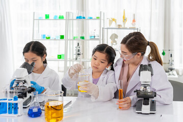 young female teacher helps kid to conduct chemical experiment with microscope,primary school...