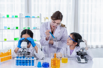young female teacher helps kid to conduct chemical experiment with microscope,primary school...