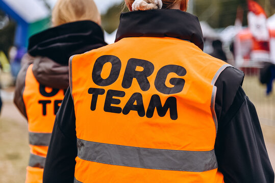 inscription ORG TEAM on back on special orange vest of young woman, organization of sports events, volunteering concept