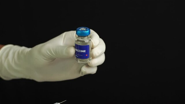 a doctor is inserting an injection into a vial containing liquid vaccine. health and medical concepts.