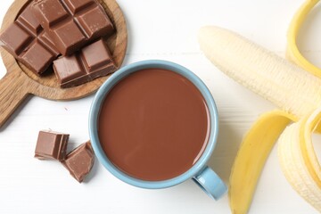 Tasty chocolate milk in cup, pieces and banana on white wooden table, flat lay
