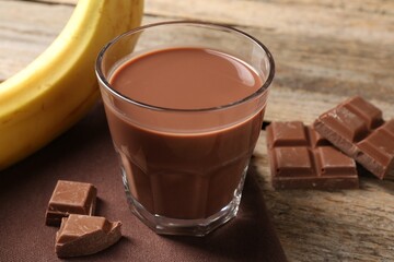 Tasty chocolate milk, pieces and banana on wooden table, closeup