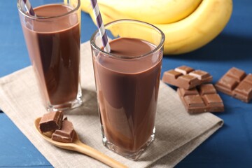Tasty chocolate milk in glasses, pieces and bananas on blue wooden table, closeup