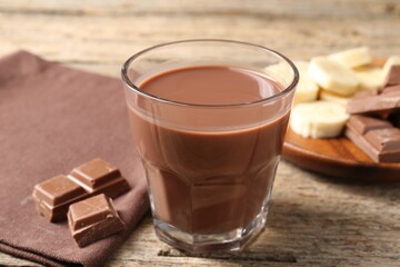 Tasty chocolate milk, pieces and banana on wooden table, closeup