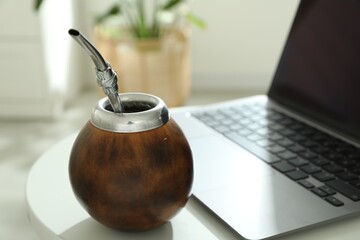 Traditional yerba mate tea and laptop on white table, closeup
