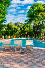 three white desk chairs or chaise lounge with blue swimming pool and hotel green garden on backgeound of vacation summer landscape