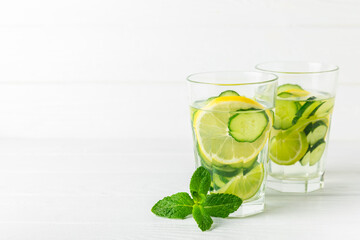 Cucumber water with lemon, lime and mint on a wooden table. Water infused with sliced ​​cucumber in a drinking glass. Tonic refreshing drink. Cucumber lemonade.Summer natural cooling drink.Copy space