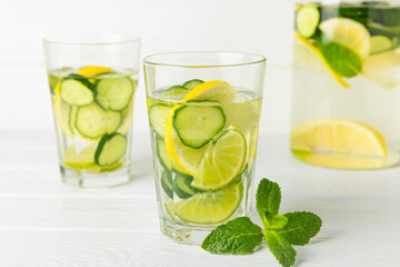 Cucumber water with lemon, lime and mint on a wooden table. Water infused with sliced ​​cucumber in a drinking glass. Tonic refreshing drink. Cucumber lemonade.Summer natural cooling drink.Copy space