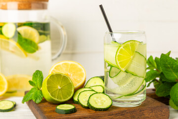 Cucumber water with lemon, lime and mint on a wooden table. Water infused with sliced ​​cucumber in a drinking glass. Tonic refreshing drink. Cucumber lemonade.Summer natural cooling drink.Copy space