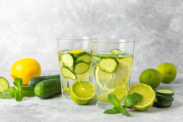 Cucumber water with lemon, lime and mint on a wooden table. Water infused with sliced ​​cucumber in a drinking glass. Tonic refreshing drink. Cucumber lemonade.Summer natural cooling drink.Copy space