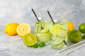 Cucumber water with lemon, lime and mint on a wooden table. Water infused with sliced ​​cucumber in a drinking glass. Tonic refreshing drink. Cucumber lemonade.Summer natural cooling drink.Copy space