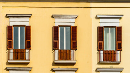 old yellow facade of house with three brown vintage wooden windows in retro italian european style