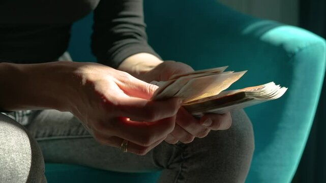 Close up woman counting British pounds in daylight near window. Hands flipping through stack of UK banknotes in soft natural light. Female managing cash finances while sitting in modern hotel room