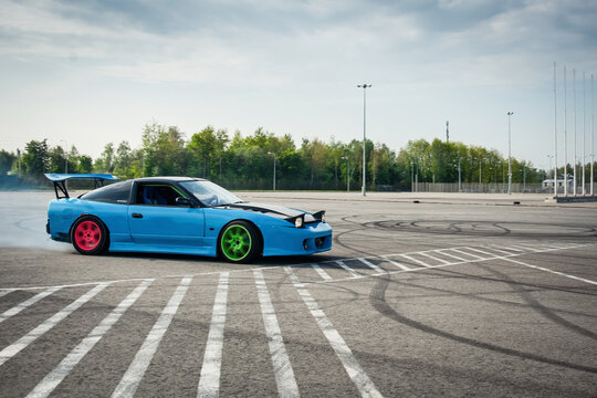 blue Nissan 200sx drifting in parking lot with smoke coming out of the rear arches. Side view of Nissan S14 powersliding on asphalt surface. Lviv, Ukraine - May 02 2014.