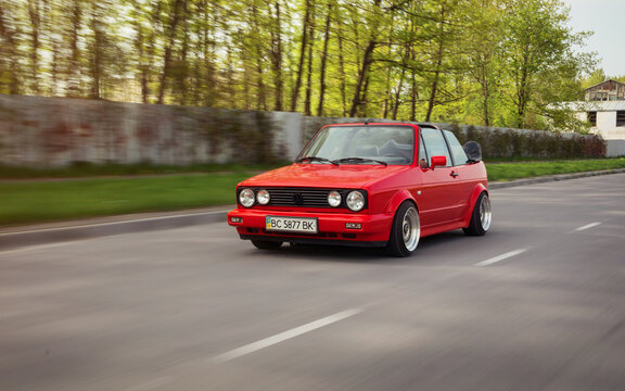 Red Volkswagen Golf mk2 cabriolet driving on a rural road. Three quarter front view of red 1980s car in countryside setting. Lviv, Ukraine - May 02 2014.