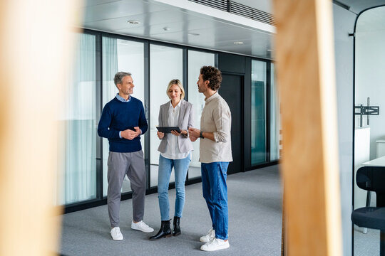 Business meeting in a modern office with three people discussing using a tablet