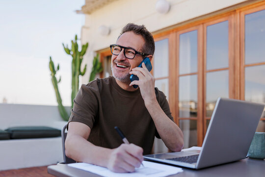 Businessman working on a laptop and talking on a smartphone on a rooftop terrace