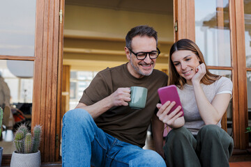 Father and daughter enjoying coffee and looking at a smartphone on a terrace