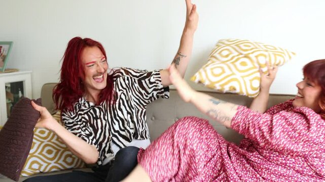 Genderfluid man and plus-size woman having fun on sofa with pillow fight