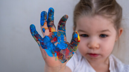 Little Girl Showing Hand Covered in Colorful Finger Paints, Smiling Playfully During Fun Creative Art Activity, Early Childhood Learning and Expression Concept