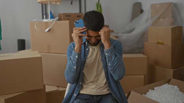Man unpacking in new home smiling holding phone surrounded by boxes in bright living room indicating successful move or joyful message
