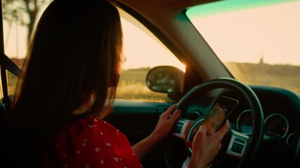 Woman using smartphone behind steering wheel at car, posing danger while driving. Distraction caused by phone usage increases risk of accidents. Staying focused on road is crucial for safety