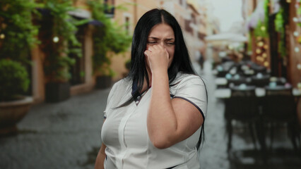 Woman standing on terrace of outdoor restaurant appearing displeased by unpleasant smell in atmosphere featuring lush greenery and cozy ambiance during daytime setting.